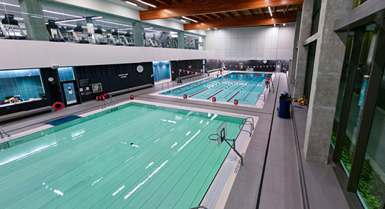 A view of two large pools in a modern indoor aquatic centre. The nearest pool has a movable floor installed.
